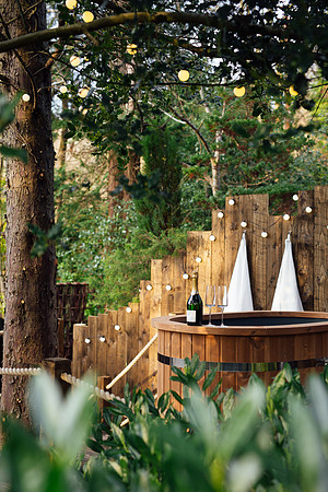 Outdoor hot tub amongst greenery and bottle of champage at Foragers cabin