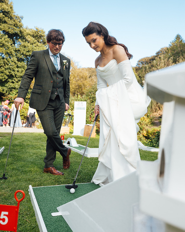 A bride & groom in designer wedding clothing play mini golf at Monkhaven Manor wedding venue