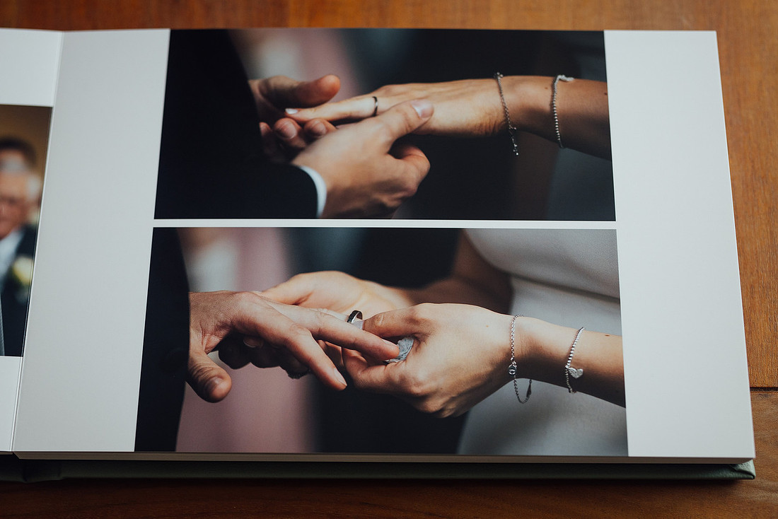An open wedding album shows bride & grooms hands exchanging rings. The high quality craftsmanship of the finished product is on display
