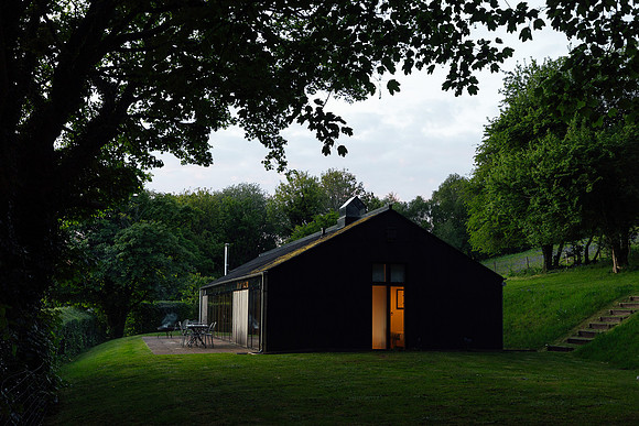 A holiday let at dusk with an overhanging tree and the lights on