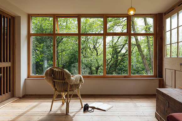 A chair looking out at a sea of green trees with a book and cup of tea