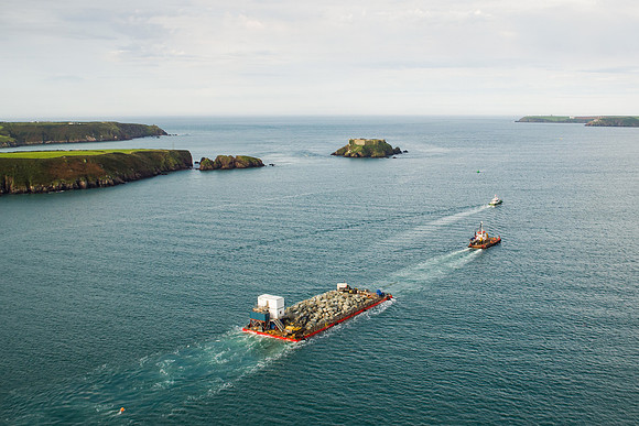 Drone image showing boulders travelling by barge out of the Cleddau estruary
