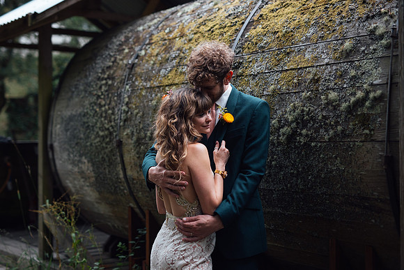 Beautiful bride and groom embrace in front of a moss covered wood structure