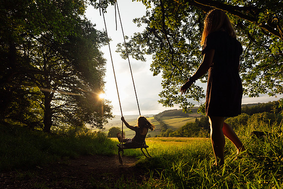 A mother pushes her child on a rope swing at sunset