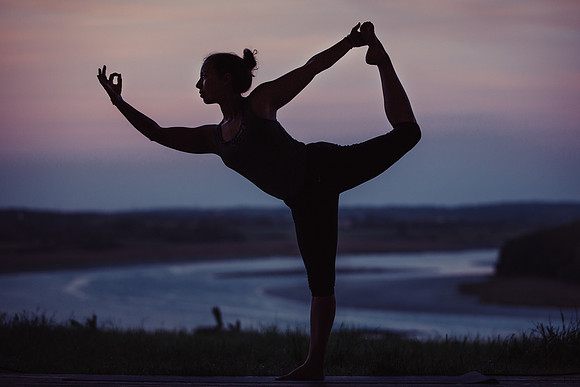 Warrior 3 yoga pose in front of a dusk sky