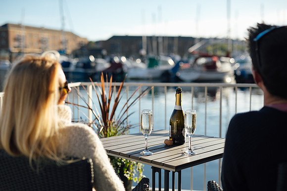 A newly wed couple look out towards the boats with a bottle of champagne