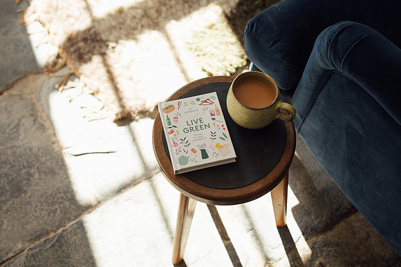 A cup of tea and Live Green book on a sidetable with window light pouring onto a stone floor